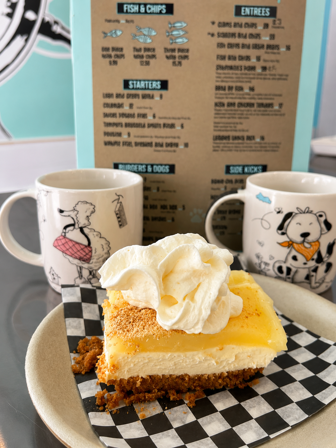 A slice of cream pie with Rudy and Olive's mugs and menu