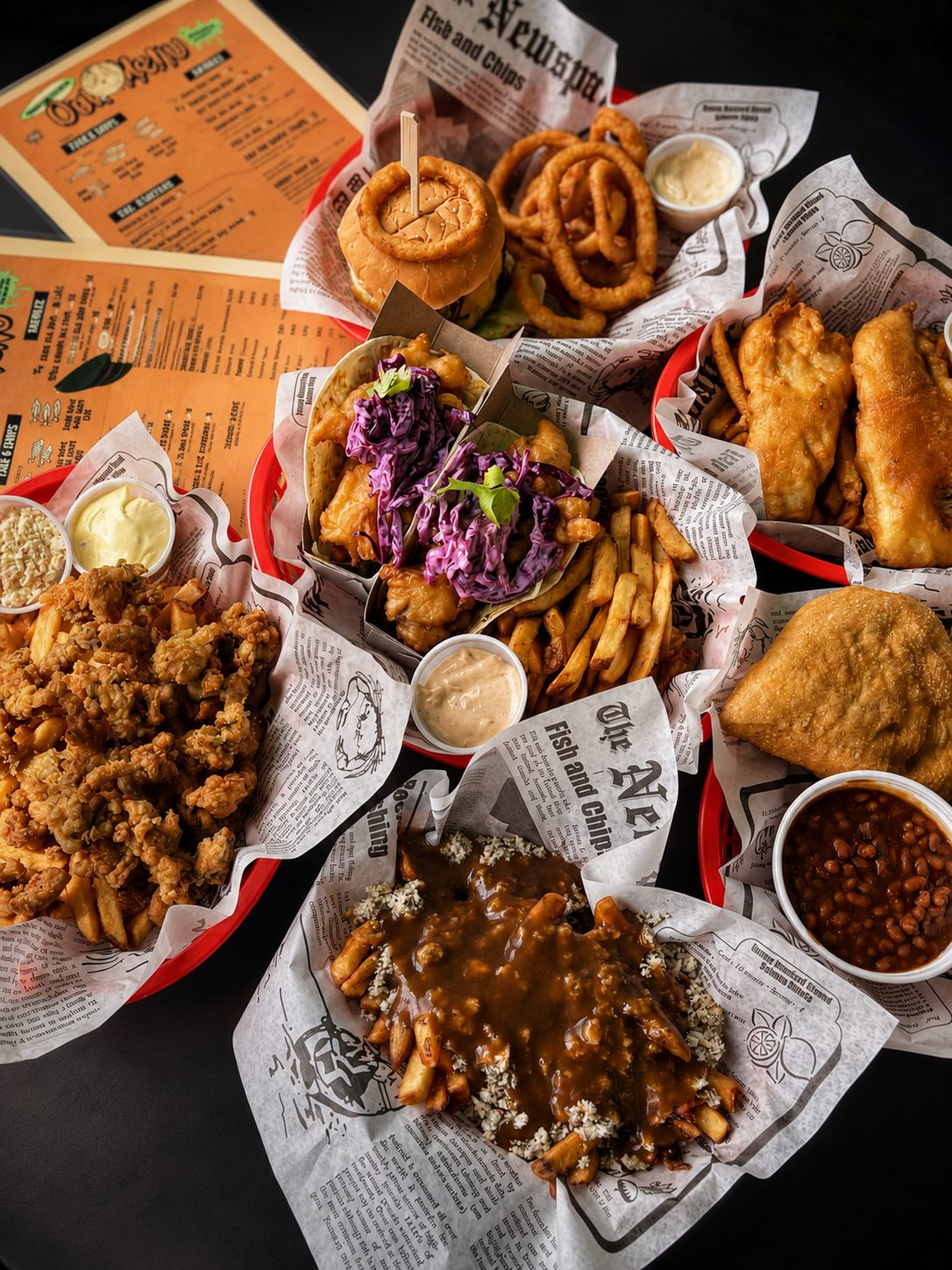 A table spread with a burger, onion rings, poutine and fish tacos